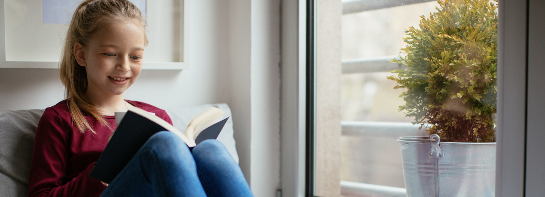 Teenaged girl reading a book by a window.